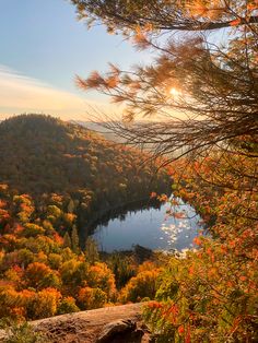 a lake surrounded by trees with fall foliage around it and the sun shining on the water