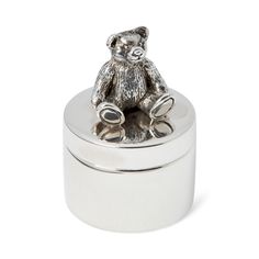 a small silver teddy bear sitting on top of a metal container with its lid open