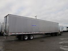 a large semi truck parked in a parking lot with other trucks behind it and cloudy skies overhead