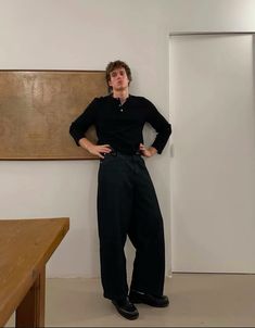 a man standing in front of a wooden table with his hands on his hips while wearing black pants