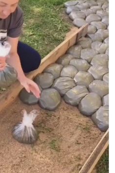 a woman kneeling down next to a pile of rocks and two bags of catnip