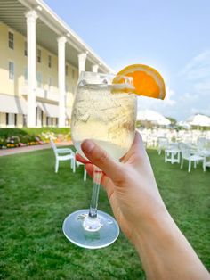 a person holding up a glass with an orange slice on it in front of a building