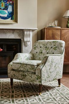 a chair sitting in front of a fireplace with a painting on the wall behind it