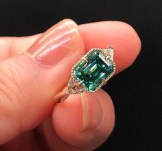 a woman's hand holding a ring with an emerald and diamond in the middle