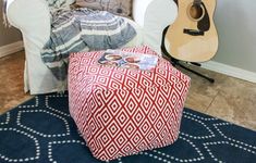 a red and white ottoman sitting on top of a blue rug next to a guitar