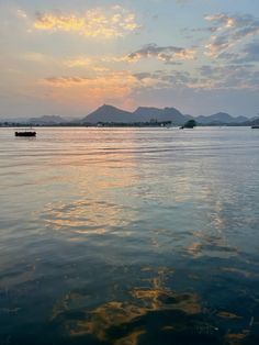 the sun is setting over the water with boats in the foreground and mountains in the distance