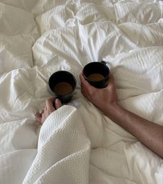 two cups of coffee are being held on the bed