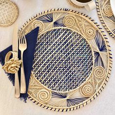 a blue and gold place setting on a white tablecloth with silverware, napkins, and cups