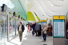 many people are walking around in an airport with signs on the walls and windows above them