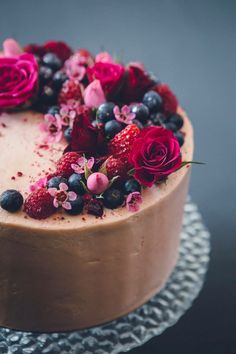 a cake with chocolate frosting and fresh berries on top is decorated with pink flowers