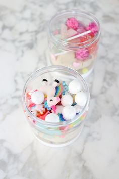 two plastic containers filled with candy and marshmallows on top of a marble counter