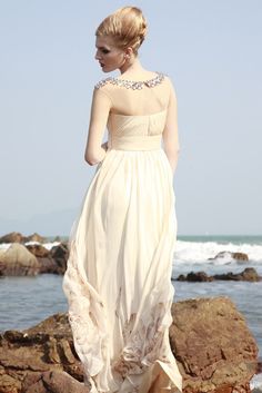 a woman in a dress standing on rocks near the ocean with her back to the camera