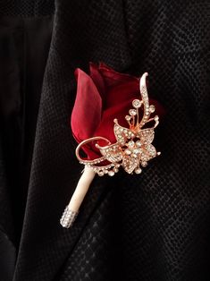 a red rose brooch sitting on top of a black jacket with crystal stones and pearls