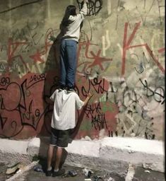 two people painting graffiti on the side of a wall