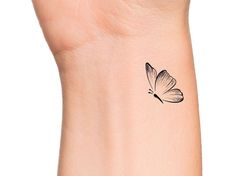 a black and white butterfly tattoo on the left side of the wrist, with one wing extended