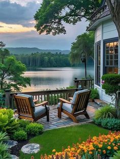 two wooden chairs sitting on top of a lush green field next to a lake at sunset