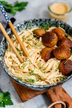 a bowl filled with pasta and meatballs on top of a wooden cutting board next to a glass of orange juice