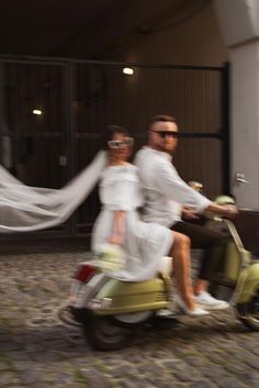 a man and woman riding on the back of a moped