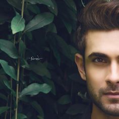 a man is posing for a photo in front of some plants and trees with his eyes wide open