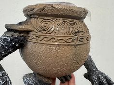 a hand holding a clay pot with designs on it's face and hands in the air