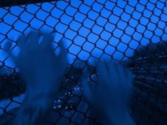 two hands touching each other over a fence with blue lights in the sky behind them