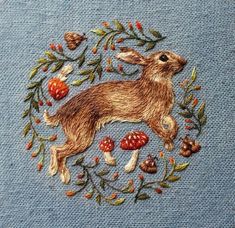 an embroidered image of a rabbit surrounded by berries and acorns on a blue background