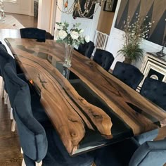 a dining room table made out of wood and blue velvet chairs with flowers in vase