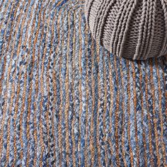 a ball of yarn sitting on top of a blue and brown striped rug next to a pillow