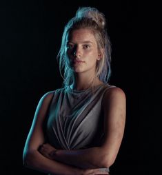 a woman standing in the dark with her arms crossed and looking off to the side