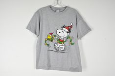 a gray t - shirt with a snoopy christmas cartoon on the front and santa's hat on the back