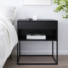 a black nightstand with magazines on it next to a bed