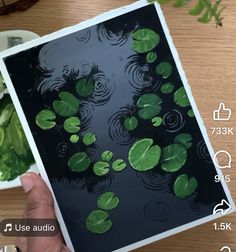 a person holding up an art piece with water lilies on it and green leaves floating in the water