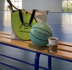 there is a bag and a basketball sitting on a bench with a cup next to it