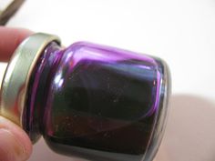 a hand holding a purple glass bottle with a metal cap on it's top