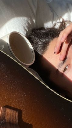 a man laying in bed with his head on the back of an acoustic guitar and looking at the camera