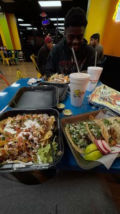 a man sitting at a table filled with tacos and other food on trays