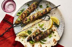 two skewered meats on a plate with lemon wedges next to them