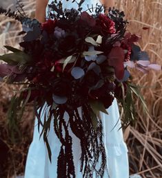 a woman holding a bouquet of flowers in front of some dry grass and plants on the ground