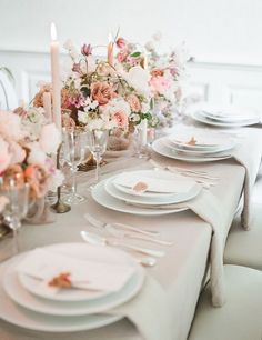 the table is set with white plates, silverware and pink flowers in vases