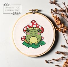 a cross stitch frog sitting on top of a mushroom