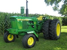 a green tractor parked in front of a corn field with two large tires on it