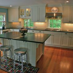 a large kitchen with an island in the middle and two stools on the floor