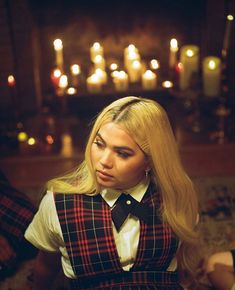 a woman with long blonde hair wearing a plaid vest and bow tie in front of candles