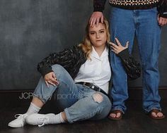 a woman sitting on the floor next to a man with his hands behind her head