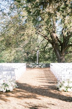 an outdoor ceremony setup with white chairs and flowers on the aisle, surrounded by trees