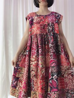 a woman standing in front of a white curtain wearing a dress with colorful flowers on it