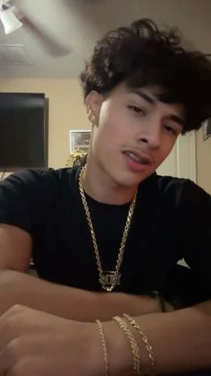 a young man sitting at a table with his arm crossed and wearing a gold chain around his neck