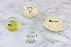 three glass bowls containing coconut oil, beeswax and olive oil on a marble countertop