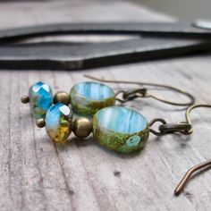 three blue and green glass beads are hanging from brass hooks on a wooden table next to a pair of scissors