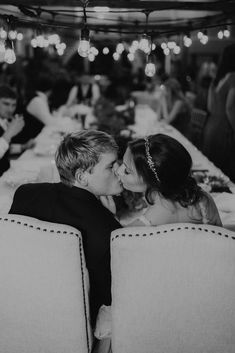 two people sitting at a table kissing each other